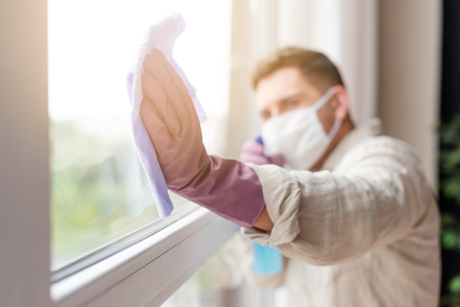 A man in protective gloves and mask cleaning a window after renovation work
