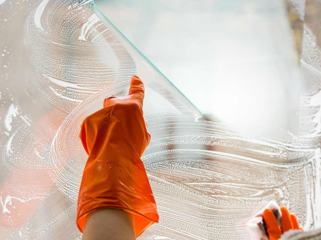 Gloved hand cleaning a window with a squeegee and soap