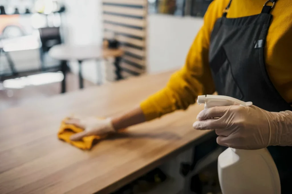 Cleaner in gloves wiping restaurant table with disinfectant spray in London bar.