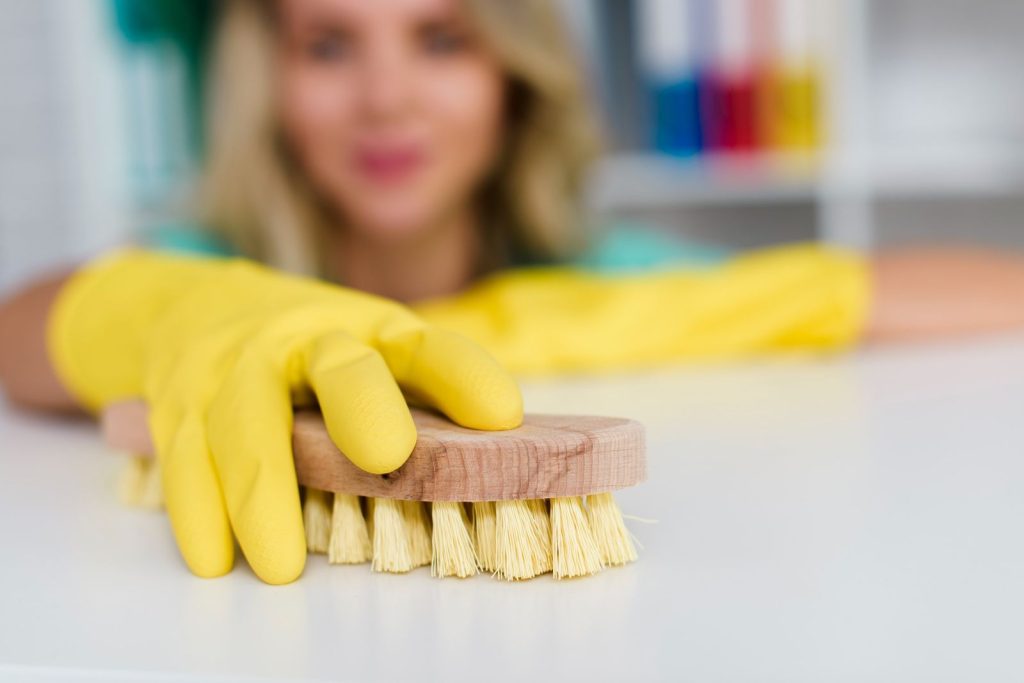Woman cleaning desk with brush in yellow gloves – Busy Bee Clean London